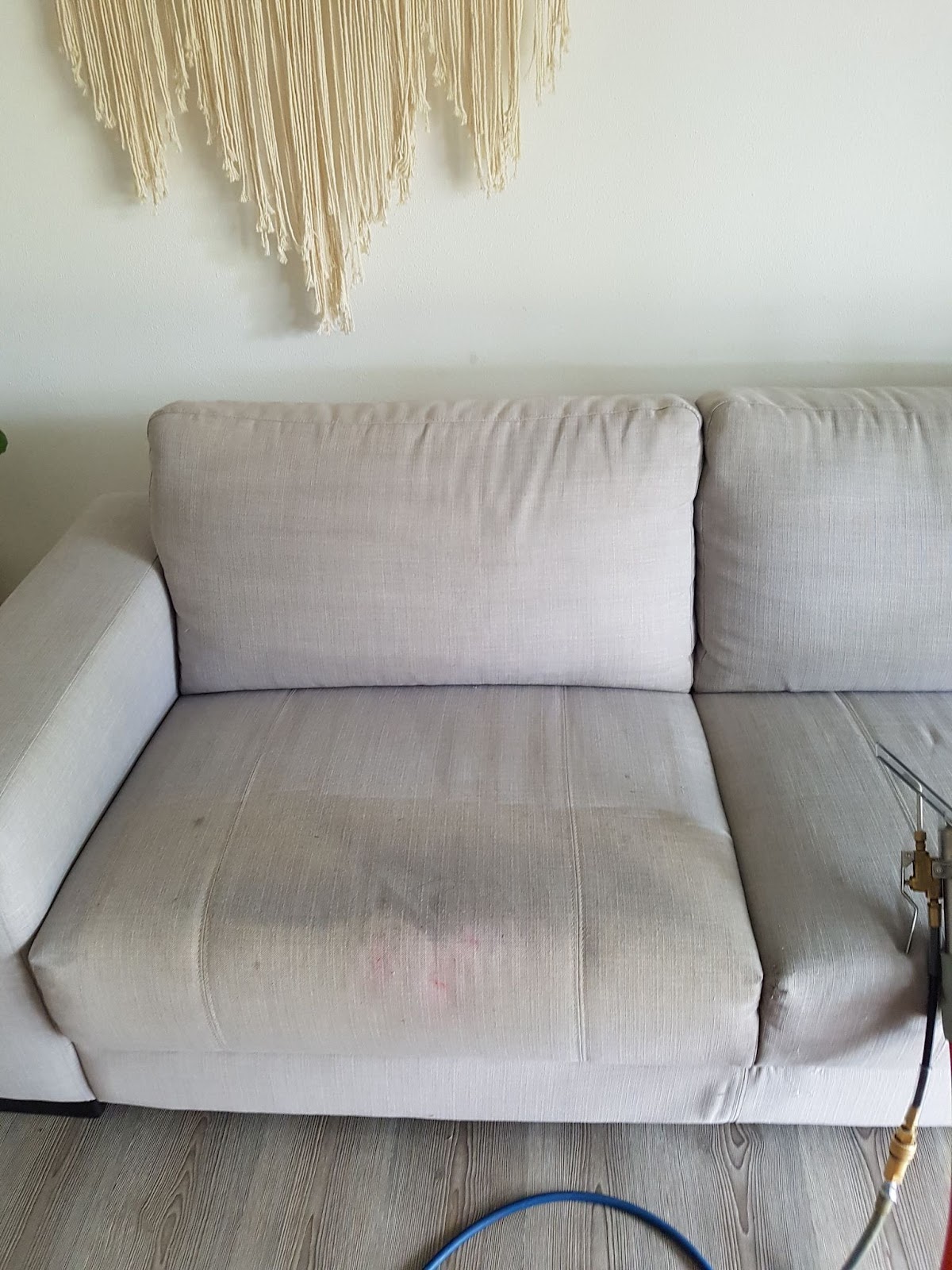 A light fabric two seater lounge with marked seat cushions, the upholstery tool beside it